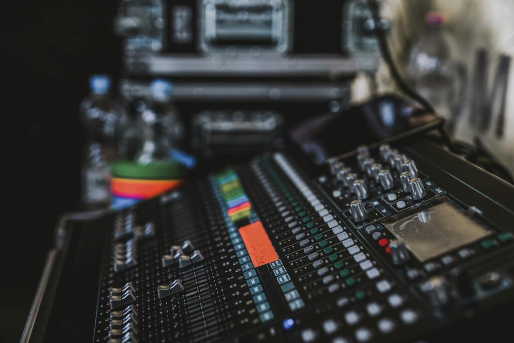 Close-up of a professional audio mixer with various knobs and sliders in a music studio setting.